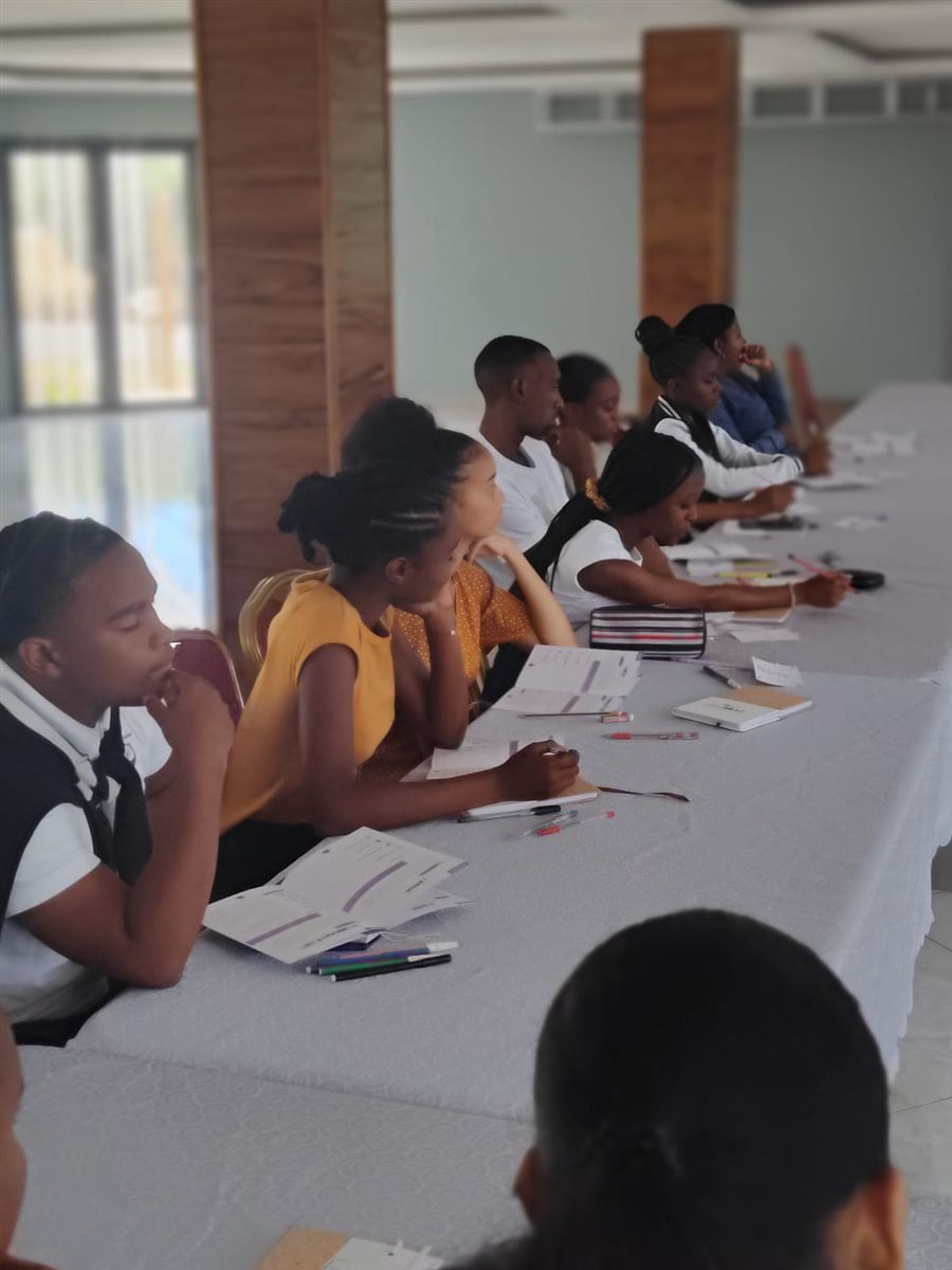 Formation des ambassadeurs à Rodrigues : des jeunes assis le long d'une grande table, fiches d'activité et stylos devant eux, écoutent attentivement