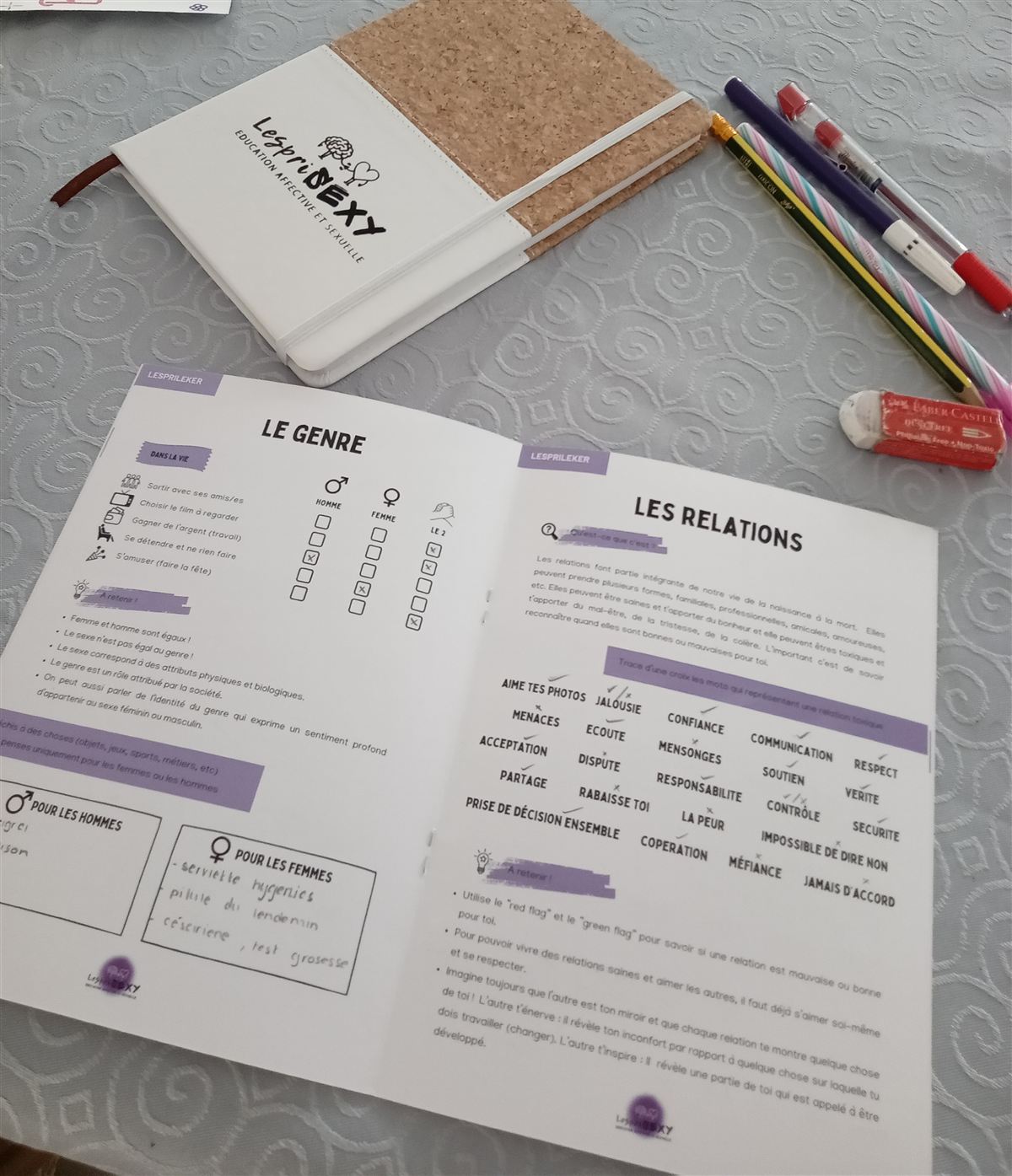 Le cahier d'exercices LespriSEXY ouvert sur une table aux pages « Le genre » et « Les relations », à côté d'un carnet LespriSEXY et de crayons