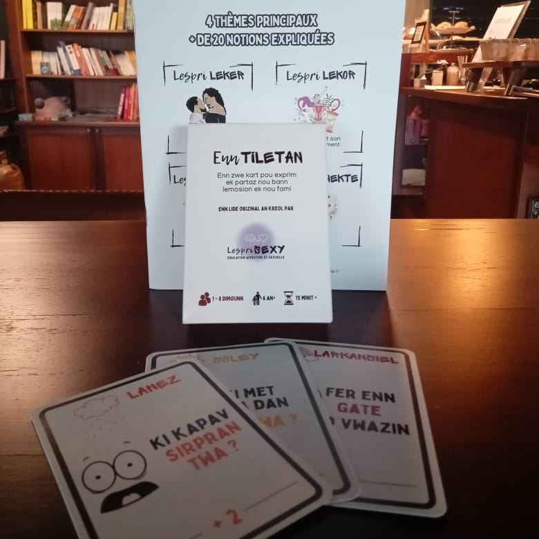Cartes Enn tiletan posées sur une table devant la boîte du jeu, avec des questions en créole comme « Ki kapav sirpran twa ? »