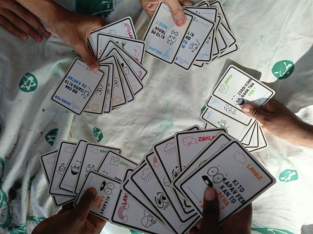 Vue de dessus : plusieurs joueurs tiennent en éventail les cartes illustrées d'Enn tiletan pendant une partie