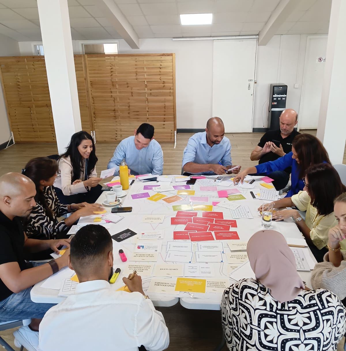 Des participants penchés sur la table organisent des cartes roses, jaunes et blanches pendant la Fresque de l'Équité