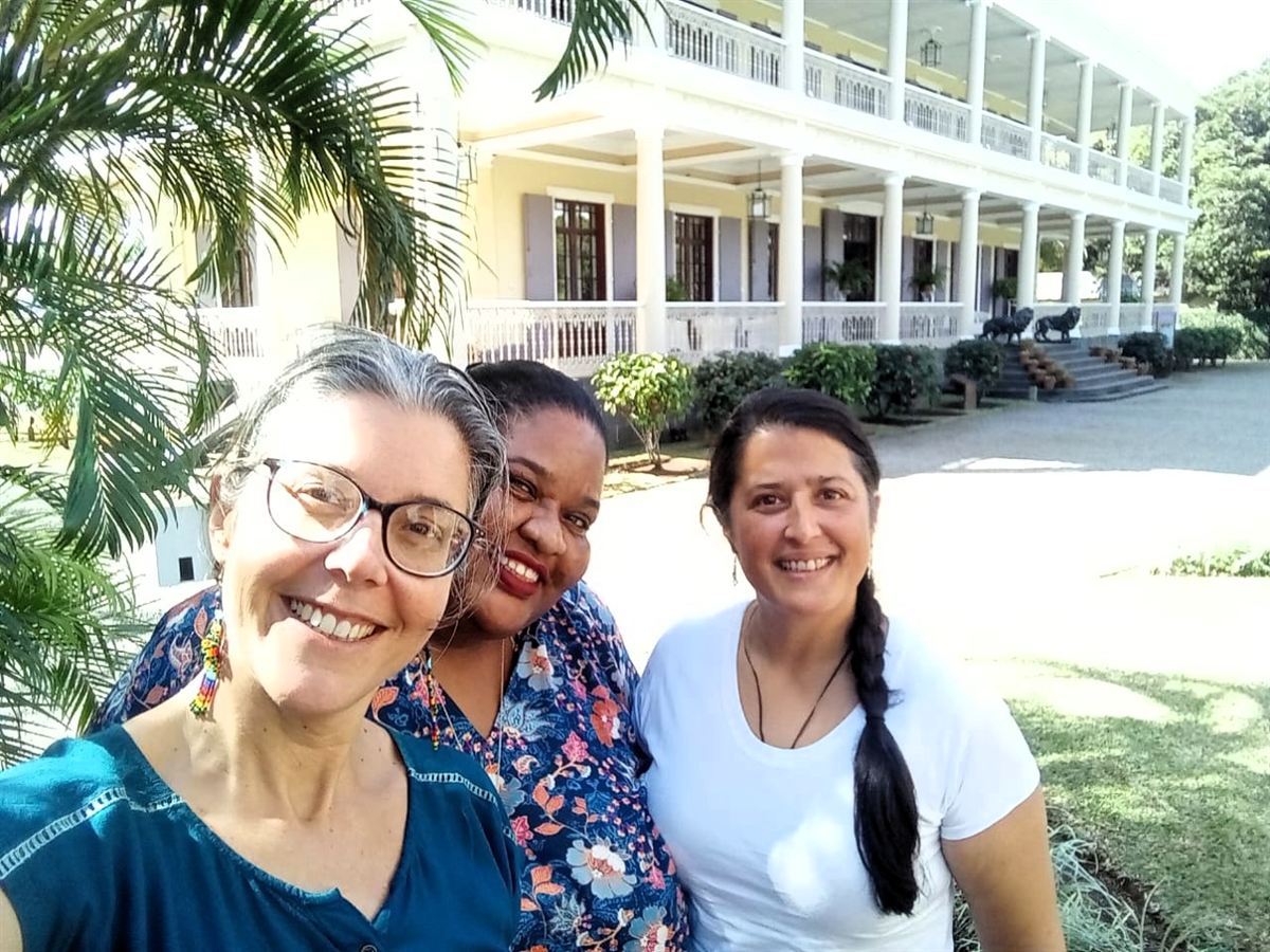 Selfie souriant de trois animatrices de l'équipe devant une grande demeure coloniale entourée de palmiers