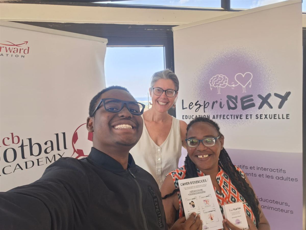 Gaëlle et deux membres de l'équipe devant les kakémonos LespriSEXY, avec le cahier d'exercices et le jeu Enn tiletan en main