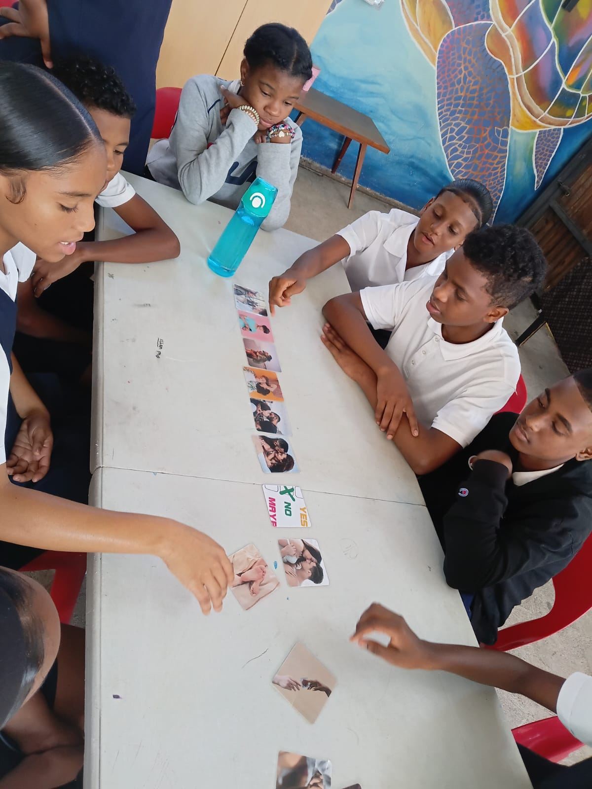 Vue de dessus : des jeunes en uniforme scolaire classent des cartes photos en ligne sur une table, à côté d'une carte « Yes, No, Maybe »