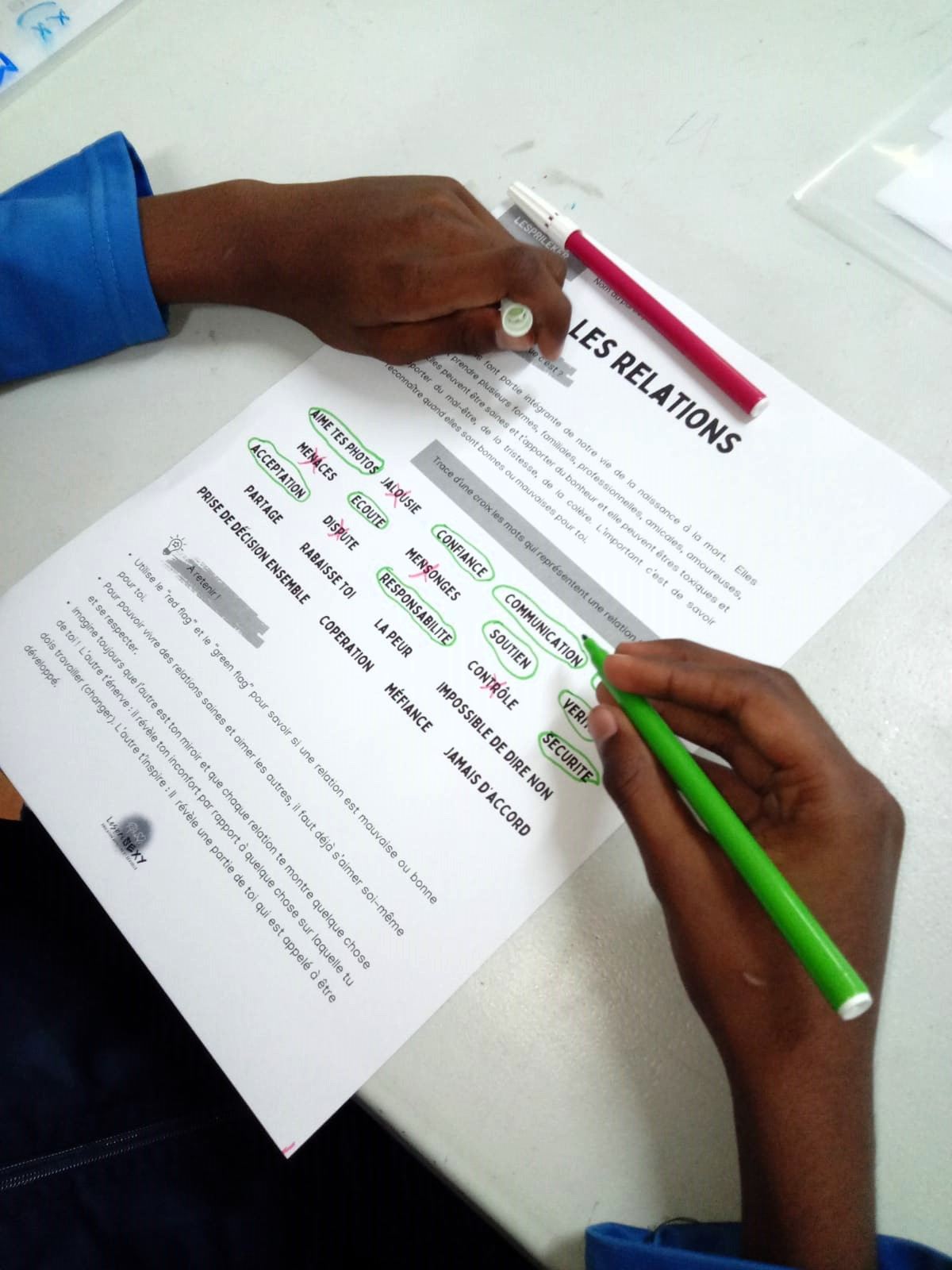 Une main entoure au feutre vert des mots sur une fiche « Les relations » : confiance, écoute, respect, contrôle